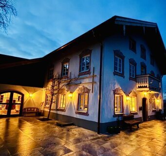 Die Alma 273 in Messing antique setzt elegante Lichtakzente an einer traditionellen Hausfassade im Landhausstil und betont Fenster, Putz und Holzdetails.