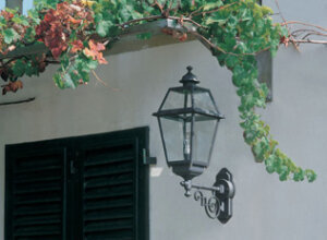 Wandleuchte außen am Eingang einer italienischen Villa. Viereckiges Gehäuse an Jugendstil Wandarm. Anthrazit, Klarglas.