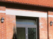 Wandleuchte flache Form mit 6 Klarglasscheiben, schwarz. Sind montiert an roter Ziegelwand, rechte und links eines weißen Fensters.