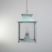 Auf dem Bild sieht man die
„Historische Außenleuchte Pétrole Nr. 1019 Géante mit Deckenkette und verdigris-Finish – französischer Stil“. Im Hintergrund eine weiße Steinmauer. Das Design ist klassisch viereckig.