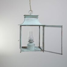Außenlampe Pétrole Géante vor weiß verputzter Steinfassade – stimmiges Gesamtbild. Man sieht die Deckenkette, die Leuchtentür ist geöffnet. Klarglasscheiben in grün-weiß patiniertem Lampengehäuse.