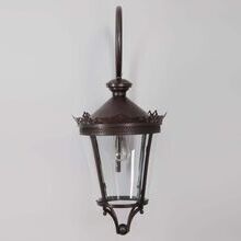 Die geschwungene Wandhalterung aus Schmiedeeisen betont das elegante Design dieser Außenleuchte. Das Lampendesign ist rund mit einem runden Lampenglas.