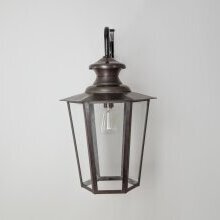 „Historische Außenwandleuchte Vaucresson XL Nr. 1121 im antiken Messing-Finish an einer weißen Hauswand montiert“. Sichtbar sind das verglaste Lampengehäuse und der Montagepunkt auf der Leuchte.