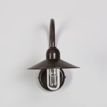 Elegante Krümmung mit nostalgischem Charakter. Tellerleuchte aus antikem Messing mit ovalem Zylinderglas. Lampe hängt an einer weißen Putzmauer.