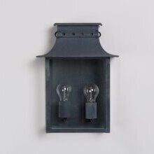 „Historische Doppelwandleuchte Longchamp Nr. 2108 L von LumArt – symmetrisches Design im gealterten Zink-Finish“Abbildung an einer hellen Hauswand.