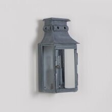 die viereckige Wandleuchte im historischen Design ist aus gealtertem Zink mit drei Lampengläsern. Montiert an einer weiß verputzten Wand.