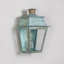 Bordeaux Wandleuchte Nr. 2136 M in Verdigris-Finish – montiert an einer weißen Putzwand mit traditionellem Fassadenprofil. Frontale Darstellung der Leuchte mit rechteckigem Glaskörper und verziertem Dachaufsatz.