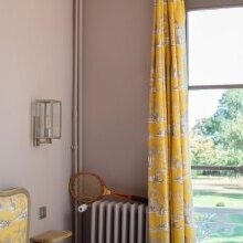 rechteckige Wandleuchte mit klaren Formen in silberem Glanz durch das gebürstete Nickel-Finish. Blick ins Zimmer und auf das Fenster.