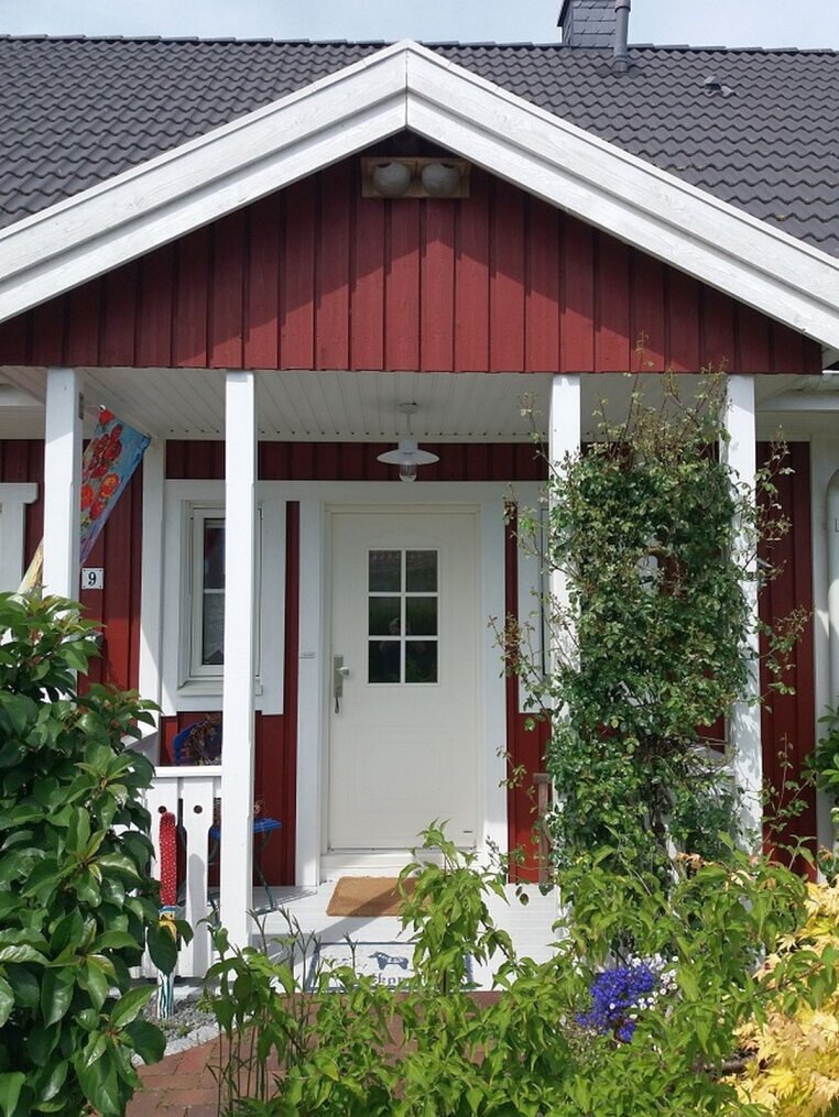 Die Deckenleuchte ist an der Decke eines roten Holzhauses angebracht. Das Dach ist grau. Die Veranda hat vier Säulen.