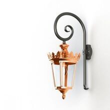 Die Wandlaterne Louvre Modell 2 besticht durch ihr zeitloses Design aus hochwertigem, vorpatinierten und lackiertem Kupfer. Der elegante Wandarm mit geschwungenem Muster harmoniert perfekt mit der goldfarbenen Krone und den klaren Glaselementen. Die Form der Laterne ist rund. Ideal für den Einsatz im Außenbereich, verleiht diese wetterfeste Lampe Ihrem Eingangsbereich, Ihrer Terrasse oder Gartenfassade einen klassischen Charme. Die Laterne wird in Handarbeit individuell hergestellt und das macht jede Laterne einzigartig.